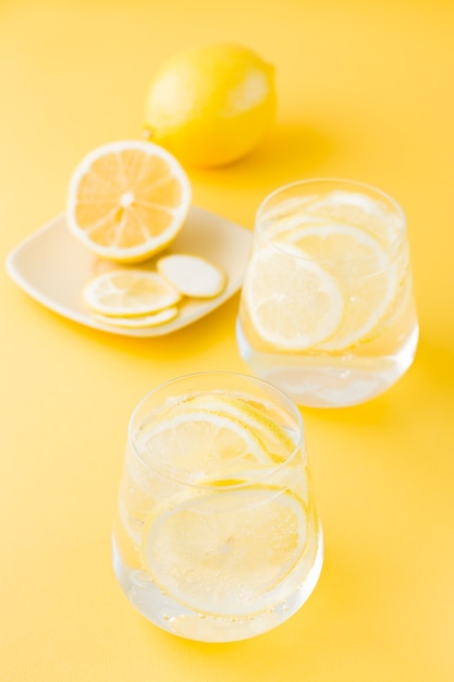 Sparkling water with lemon and ice in glasses and lemon slices on a saucer on a yellow