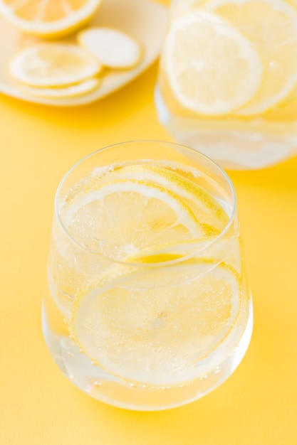 Sparkling water with lemon and ice in glasses on a yellow table.