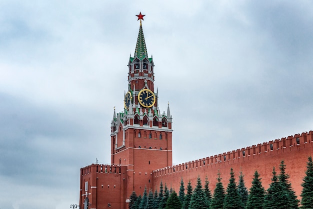 Torre spasskaya del cremlino con bellissimi abeti blu sulla piazza rossa di mosca contro un cielo cupo.