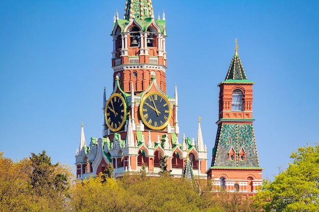 Spasskaya tower of Moscow Kremlin against green trees and blue sky