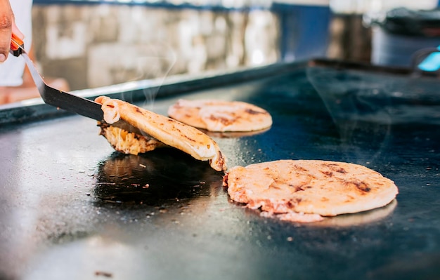 Spatel die een traditionele kaaspupusas op de grill neemt Close-up van traditionele ambachtelijke gegrilde pupusas Traditionele Nicaraguaanse pupusas met gesmolten gegrilde kaas