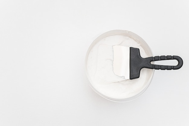 Spatula and a bucket of putty on white wooden boards.