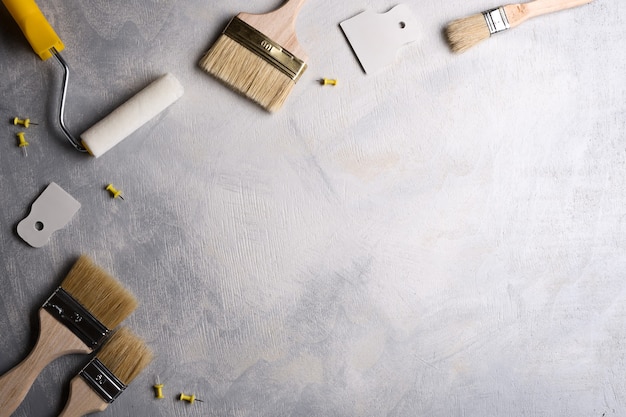 Spatulas for application of putty and brushes and rollers for painting on a gray concrete background . Top view