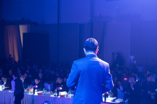 Speaker on stage and giving talk at business meeting. Audience in the conference hall.