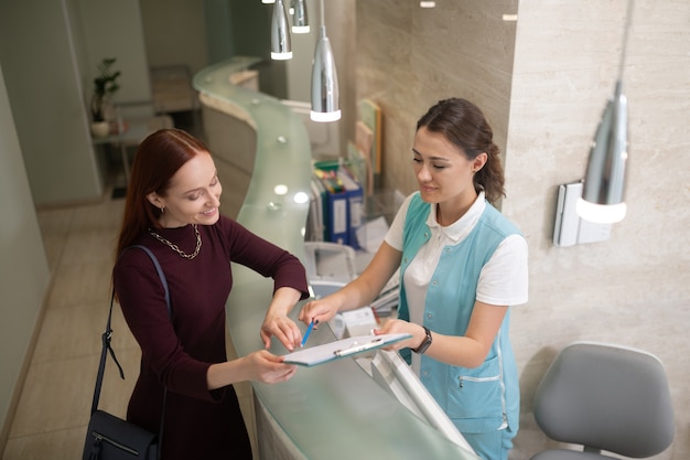 Speaking with receptionist. Smiling mother speaking with receptionist in private dentistry before examination