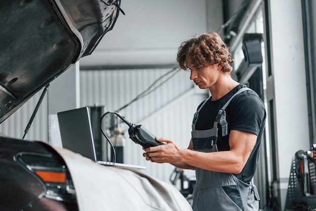 Speciaal hulpmiddel voor het testen van kenmerken Volwassen man in grijs gekleurd uniform werkt in de autosalon