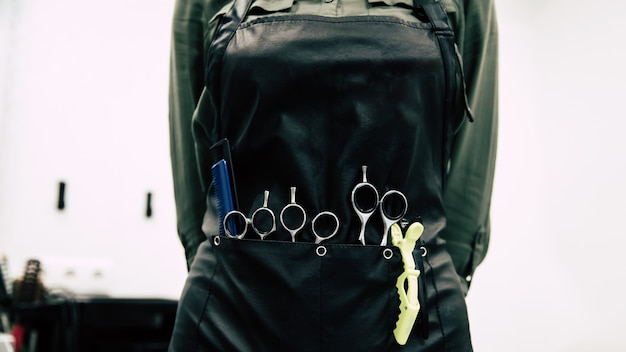 Special equipment for a hairstyle.Â  Low angle view of female hairdresser posing in hairdresser apron with hair styling tools in pockets.