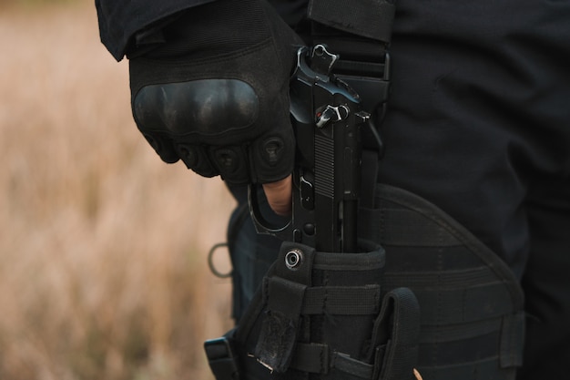 Foto soldato delle forze speciali in uniforme nera che tira una pistola dalla sua fondina