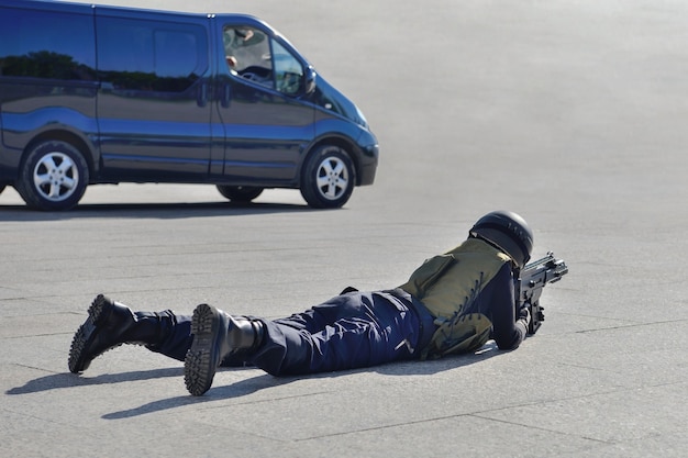 Special forces soldier lying on the ground aiming from an assault rifle near the car