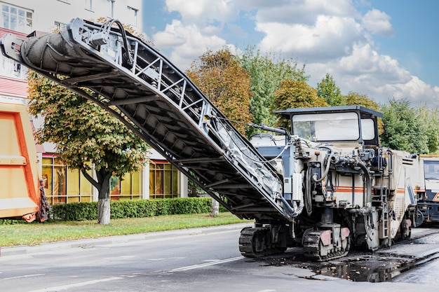 A special machine cuts the asphalt. The technician removes the old asphalt and loads it into a dump truck. Road repair, asvalt replacement, construction work.