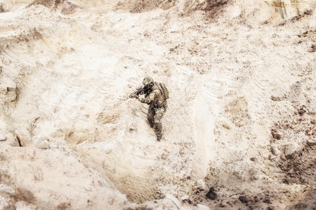 Special operations forces soldier, US army infantryman carefully sneaking, walking with service rifle in hands in hot sandy and rocky area. Military mission on Meddle East, modern warfare in desert