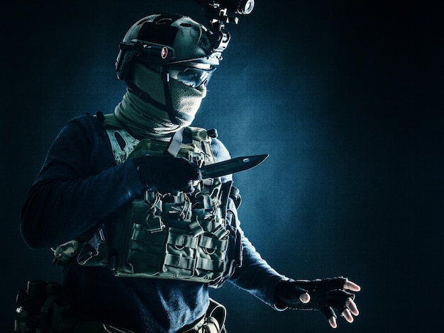 Special operations soldier commando fighter modern warfare combatant in combat uniform helmet with nightvision wearing mask and glasses sneaking in darkness for sentry quiet removal with knife