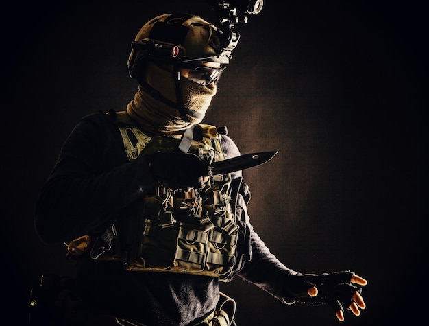 Special operations soldier commando fighter modern warfare\
combatant in combat uniform helmet with nightvision wearing mask\
and glasses sneaking in darkness for sentry quiet removal with\
knife