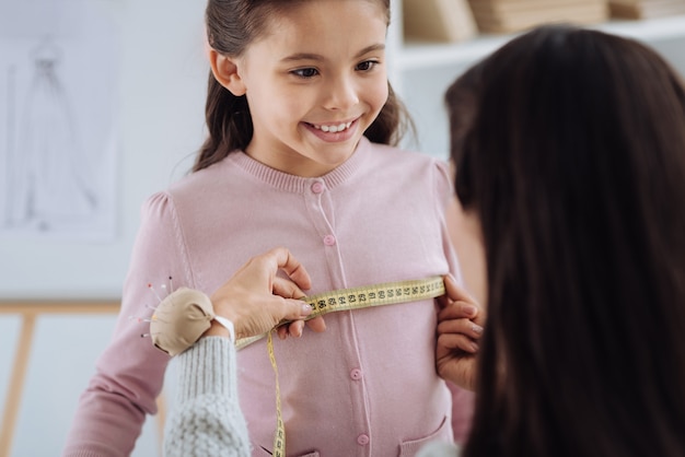 Special outfit. Nice professional female tailor using a measure tape ad making measurements for her while preparing a surprise