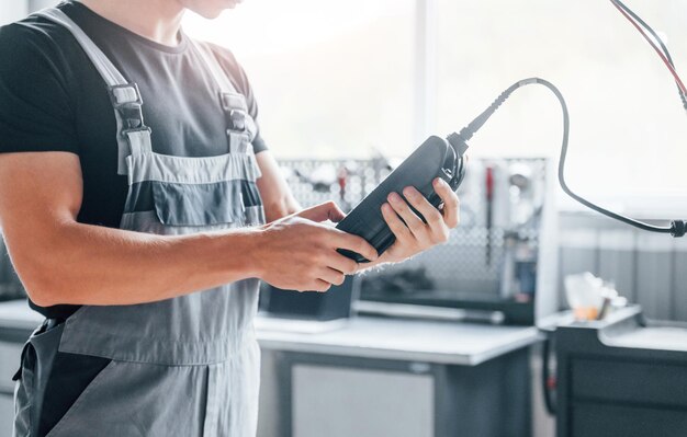 Special tool for testing characteristics Adult man in grey colored uniform works in the automobile salon