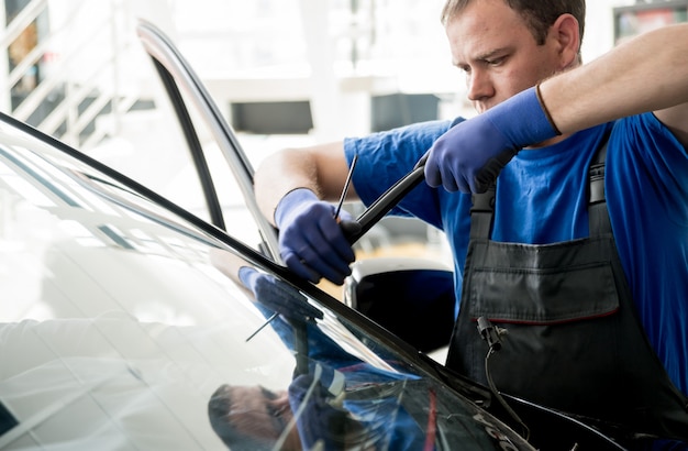 Speciale automobielarbeiders verwijderen oude voorruit of voorruit van een auto in de garage van het autobenzinestation.