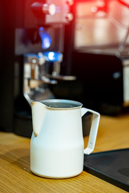 Speciale kan die aan tafel staat en zich voorbereidt op het gieten van warme melk uit de koffiemachine Verse koffie maken met melk Proces van cappuccinobereiding Close-up