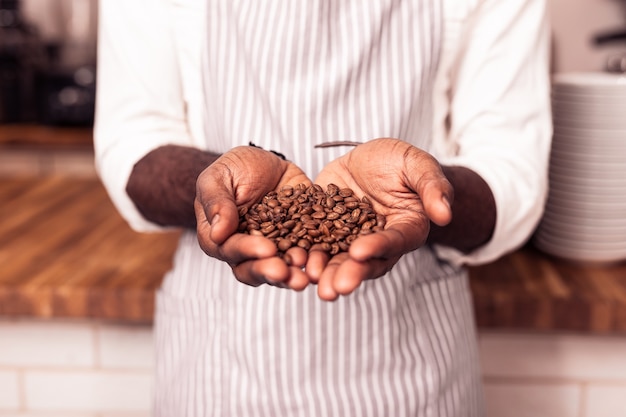 Speciale koffie. Leuke professionele barista die gebrande koffiebonen vasthoudt terwijl hij ze aan je laat zien