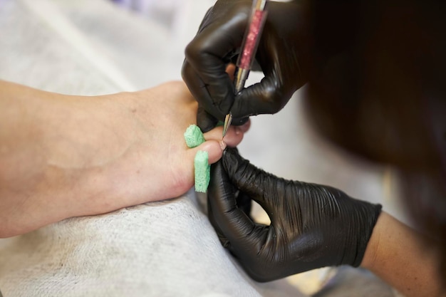 A specialist in black gloves in a beauty salon does a French pedicure for a client