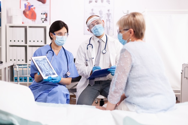 Specialist doctor and nurse presenting diagnosis to senior woman on tablet pc in time of covid19 pandemic