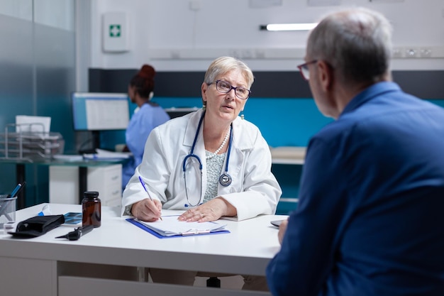 Specialist doing signature on checkup files to give prescription treatment to ill man. Woman doctor signing documents after healthcare consultation, giving medicine to old patient.