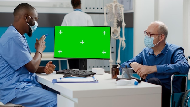 Specialist en oude man kijken naar monitor met greenscreen, omgaan met chronische stoornissen. analyse van lege mockup-sjabloon met geïsoleerde chromakey-weergave en copyspace. statief geschoten.