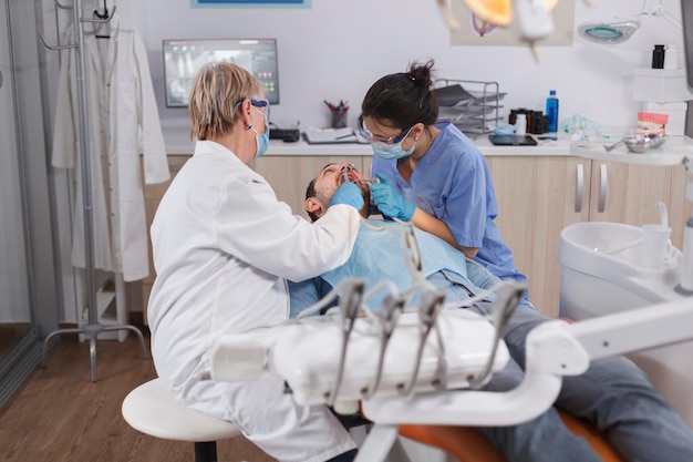 Specialist orthodontist team checking man danture analyzing teeth infection discussing patient oral hygiene during dental examination in stomatological office. Concept of stomatology medicine