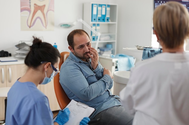 Photo specialist orthodontist team explaining oral hygiene to patient with toothache discussing medical expertise during stomatological consultation in dental office. concept of medicine service
