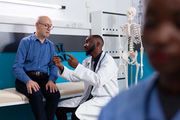 Specialist physician doctor holding lungs radiography discussing disease symptoms with retired old man explaining healthcare treatment in hospital office. Senior patient having medical appointment