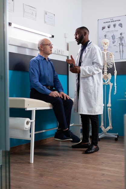 Specialist physician doctor holding pills bottle explaining medication treatment to pensioner man patient discussing disease symptoms during medical consultation in hospital office. Medicine concept