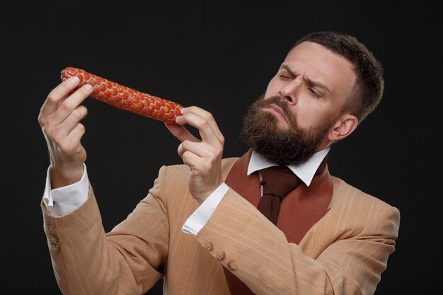 A specialist in the quality of meat products presents ham sausage with emotion on a dark background