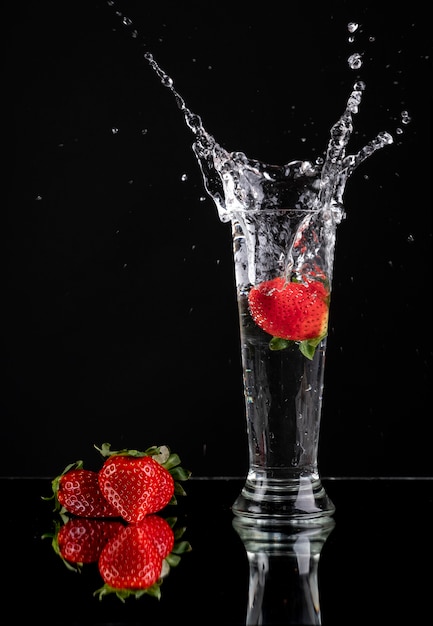 Spectacular splash of a strawberry in a glass with three strawberries next