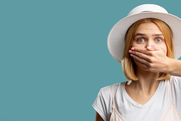 Speech freedom Female rights Scared woman in white closing mouth hand looking at camera isolated on blue copy space Keep secret Advertising background