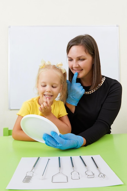 Speech therapist working with little girl in office training pronunciation