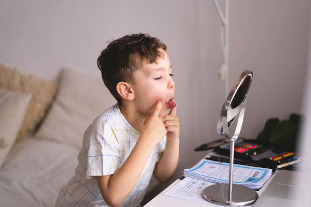 Speech therapy concept Cute little boy pronouncing sound O looking at mirror doing an online Speech therapy lesson through a laptop