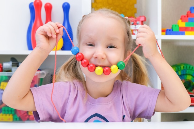 言語療法、細かい運動能力の発達。幼児の女の子がひもにビーズをひもでつないでいます。