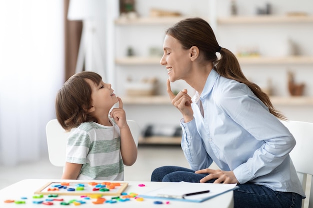 Photo speech training for kids professional woman training with little boy at cabinet teaching right