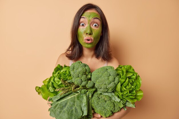 Speechless surprised asian woman carries green vegetables uses
healthy products for making beauty mask stares with omg expression
takes care of facial skin poses indoors cosmetology concept