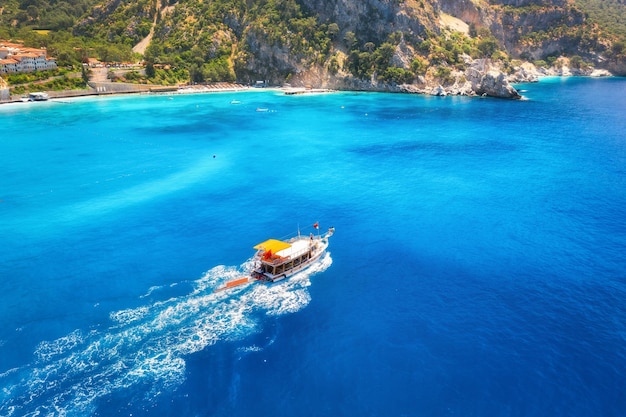 夏の日の出の青い海のスピードボート海湾に浮かぶモーターボートの空撮ヨットのある熱帯の風景澄んだ水岩石山の緑の木々上面図オルデニズトルコ