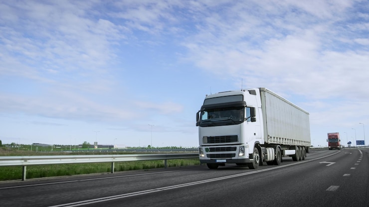 高速の白いセミトラックと貨物トレーラーが高速道路を走る トラックが重型車両の列で1位です 太陽が輝いています