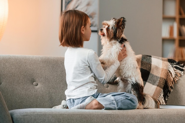 Foto speel op de bank het kleine meisje is thuis met een leuke hond