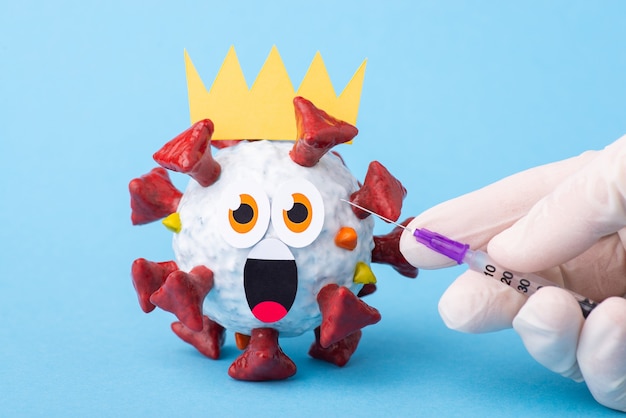 Speelgoedmodel van coronavirus met bang gezicht - ronde ogen en geopende mond, wachtend op een injectie