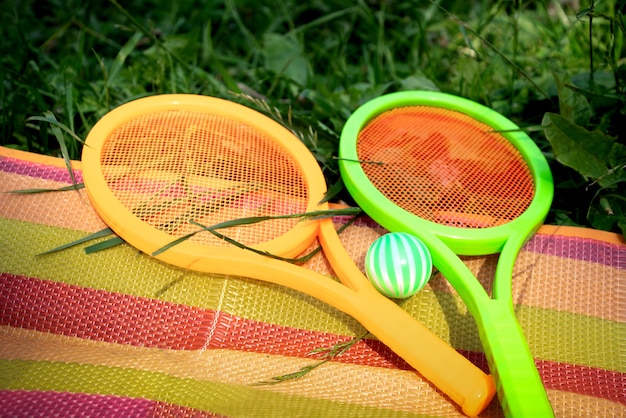 Foto speelgoedtennisrackets met bal liggend op kleurrijke gestreepte deken uitgespreid op het gras