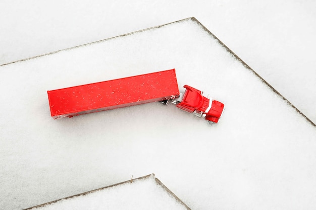 Foto speelgoedvrachtwagen in rode machine rijdt op houten vloeren en sneeuw terwijl de weg afslaat op nieuwjaarsvakantie