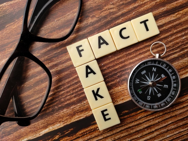 Speelgoedwoord met tekst fake fact met bril en kompas op een houten achtergrond