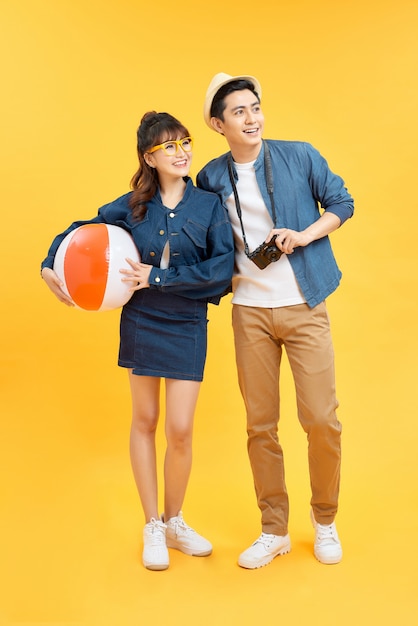 Speels Aziatisch paar in zomerse casual kleding met strandaccessoires studio-opname geïsoleerd op gele achtergrond