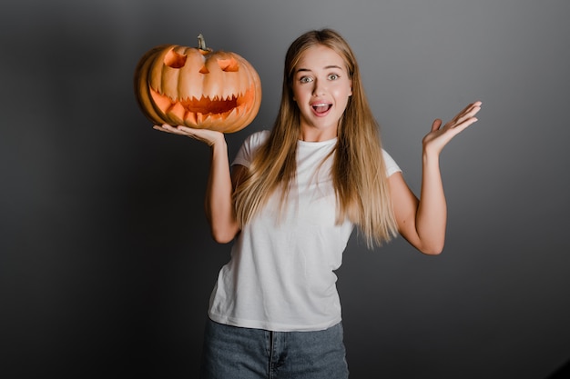 Speels grappig blondemeisje met Halloween-de pompoen van de hefboomo lantaarn die over grijs wordt geïsoleerd