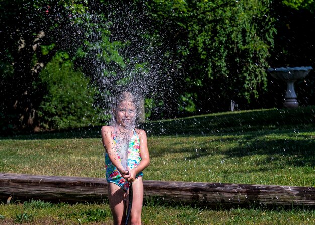 Speels meisje in zwembroek die water spuit met een tuinslang op het gazon