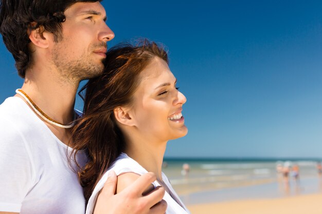 Speels paar op het oceaanstrand dat van hun zomervakantie geniet, omhelst hij haar