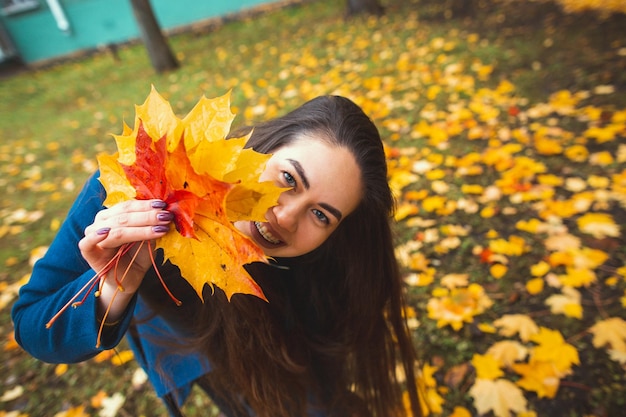 Speelse jonge vrouw met herfstbladeren in de hand en herfst gele esdoorn tuin achtergrond